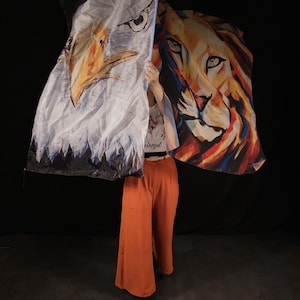 May include: A person holding two fabric flags. One flag features a white eagle with a black and blue background. The other flag features a colourful lion with a red, orange and yellow background.