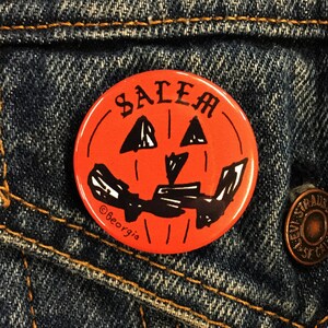 May include: Orange and black Halloween button with a jack-o'-lantern face and the word "SALEM" written across the top. The button has a copyright symbol and the text "@Beorgia" at the bottom.