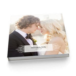 May include: A white wedding album with a photo of a couple on the cover. The album is 12 inches by 12 inches and has 15 spreads. The cover is a flush-mount lay-flat style with a "Bohemian Lace" design. The text on the cover reads "Michael & Emily" and "July 10, 2016".