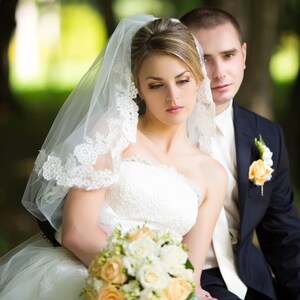 Pu&ograve; includere: Un ritratto di matrimonio di una sposa e uno sposo in un parco. La sposa indossa un abito da sposa bianco con un velo e un bouquet di fiori bianchi e gialli. Lo sposo indossa un abito scuro e una camicia bianca con una cravatta.