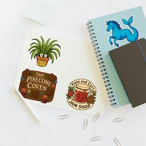 Puede incluir: Una colección de pegatinas coloridas con varios diseños. Una pegatina muestra una planta sonriente en una maceta con el texto "CAZ". Otra muestra "The Pinecone Coven" con piñas y flores. Otras pegatinas incluyen un tarro de mermelada y un caballito de mar azul.