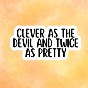 May include: A sticker featuring the phrase "CLEVER AS THE DEVIL AND TWICE AS PRETTY" in black, bold lettering. The text is on a white background, set against an orange and yellow watercolour background.