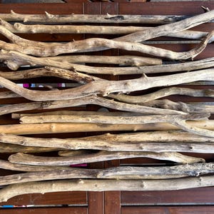 Könnte beinhalten: Eine Sammlung verwitterter Treibholzäste unterschiedlicher Länge und Dicke. Die Äste sind hellbraun und grau, mit einer natürlichen, organischen Textur. Sie sind auf einer dunkelbraunen Holzoberfläche angeordnet.
