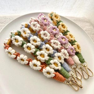 Peut inclure: Plusieurs bracelets de macramé faits à la main, ornés de fleurs en forme de marguerites. Les bracelets présentent une variété de couleurs, dont le blanc, le jaune, l'orange, le vert, le bleu et le rose. Des fermoirs dorés sont attachés à chaque bracelet.
