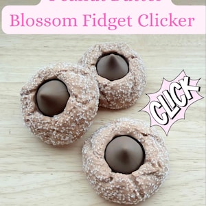 Puede incluir: Tres clickers fidget de flor de mantequilla de maní con un centro marrón y un exterior texturizado de color beige. La imagen incluye el texto "Peanut Butter Blossom Fidget Clicker" en una pancarta rosa y un gráfico "CLICK".