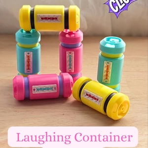 Op de afbeelding: Kleurrijk klikspeelgoed in geel, roze en blauwgroen, met zwarte en paarse accenten. Elk speelgoed heeft een rechthoekig venster met een ontwerp. De afbeelding bevat de tekst "Laughing Container Clicker" en een "CLICK"-afbeelding.