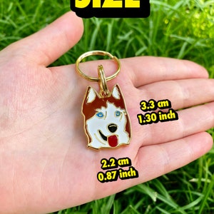 K&ouml;nnte beinhalten: Goldfarbener Schl&uuml;sselanh&auml;nger aus Metall mit einem roten und wei&szlig;en Husky-Hund mit blauen Augen. Der Schl&uuml;sselanh&auml;nger ist 3,3 cm (1,30 Zoll) hoch und 2,2 cm (0,87 Zoll) breit.