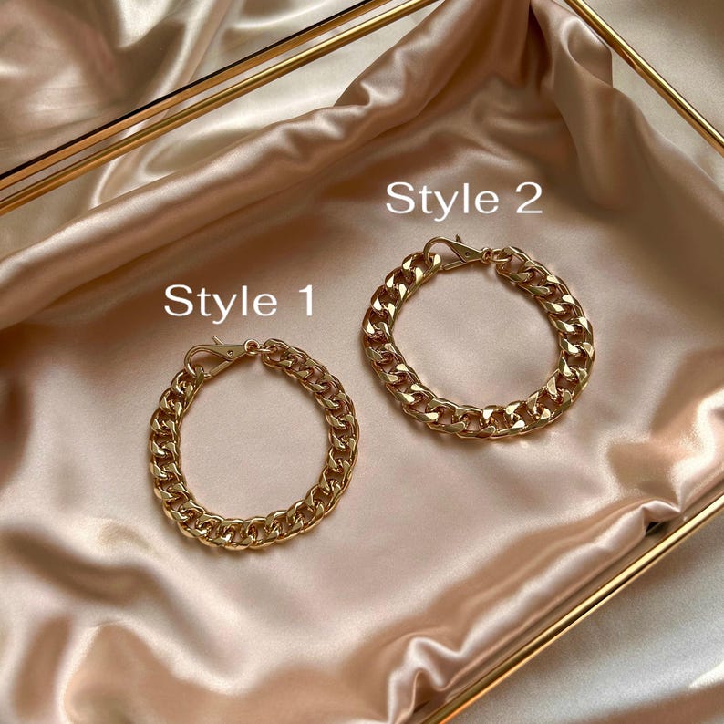 May include: Two gold-toned metal chain bracelets with lobster claw clasps. The bracelet labeled Style 1 features a smaller link design, while the bracelet labeled Style 2 features a larger, thicker link design. Both items are metallic gold.
