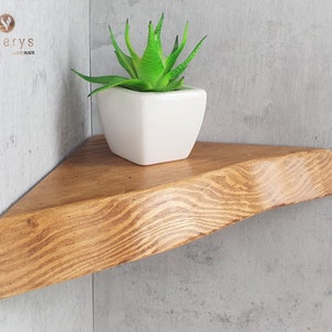 May include: A triangular wooden shelf with a natural wood finish. The shelf is mounted on a corner wall and has a small succulent plant in a white ceramic pot on top.