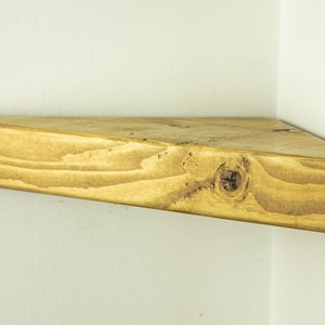 Peut inclure: Une &eacute;tag&egrave;re triangulaire en bois avec une finition en bois naturel. L'&eacute;tag&egrave;re a un bord arrondi et est mont&eacute;e dans un coin.