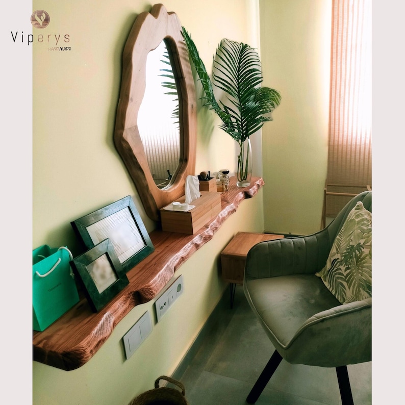 Extra live edge rustic wooden floating shelf in hallway or vanity setup. Solid wood with natural organic edge, mounted under mirror and decorated with plants, tissue box and picture frames. Sustainable handmade wall decor & storage.
Rustikale Wandregal mit natürlicher Baumkante, ideal für Flur oder Schminktisch.
Étagère murale rustique en bois massif avec bord naturel, déco pratique et artisanale.