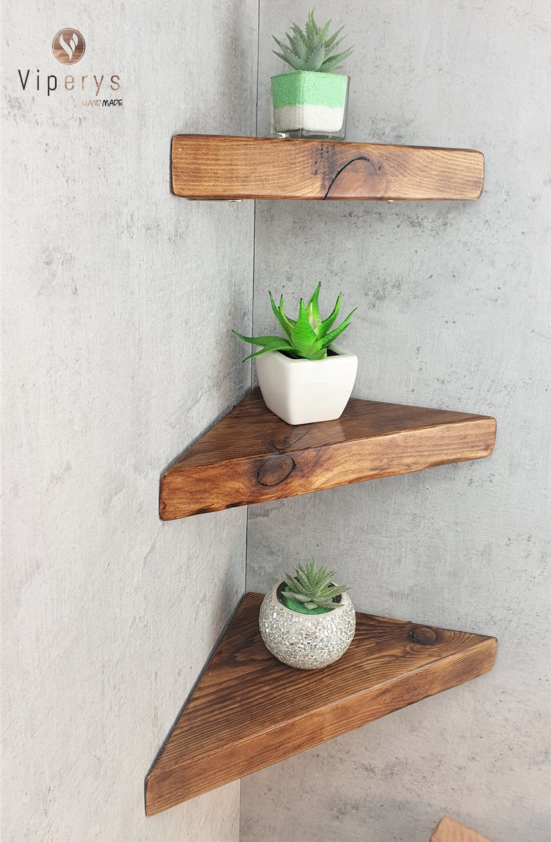 May include: Three wooden corner shelves with triangular shapes. The shelves are stained a dark brown color and are mounted on a light gray wall. Each shelf has a small potted succulent plant on it.
