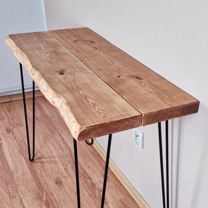 May include: A wooden table with a live edge top and black hairpin legs. The table is made of natural wood and has a rustic look.