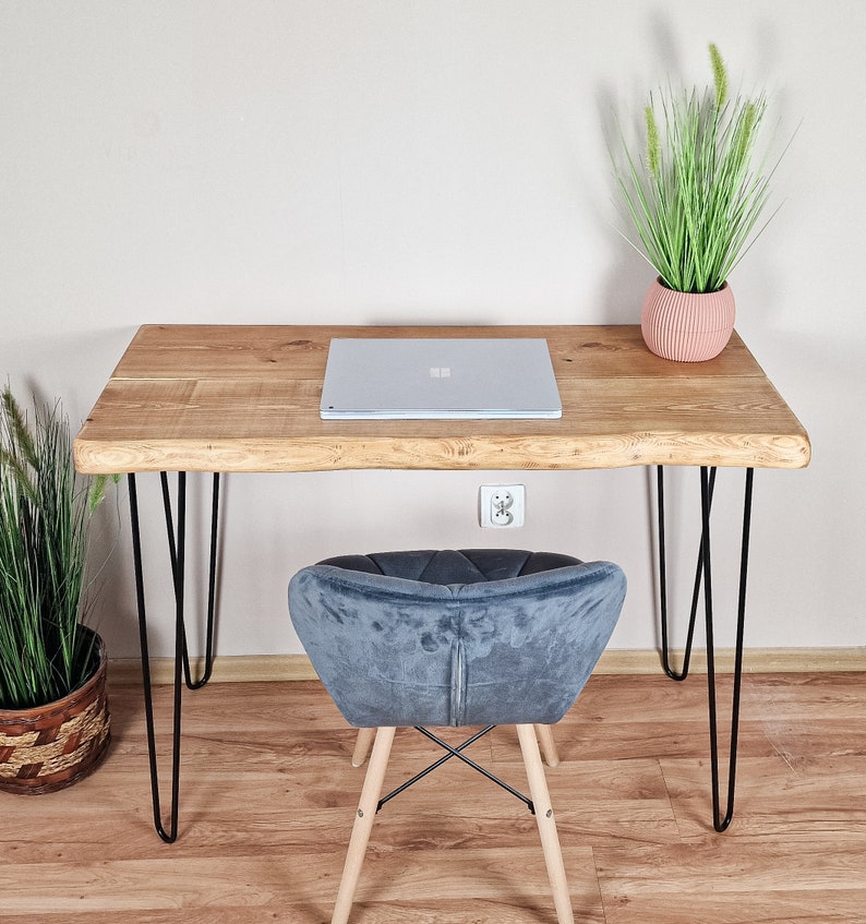 May include: A light wood desk with a live edge top and black hairpin legs. A laptop computer is on the desk, and a blue velvet chair is in front of the desk. A potted plant is on the desk.