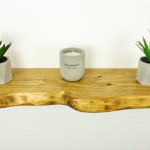 Side view of thick extra live edge rustic shelf highlighting wood texture and natural imperfections. Floating handmade shelf, sustainable solid wood.
Seitenansicht des dicken Wandregals mit sichtbarer Holzstruktur und natürlichen Unregelmäßigkeiten.
Vue latérale de l'étagère épaisse en bois rustique avec détails naturels, artisanat durable.