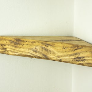 May include: A rustic wooden corner shelf with a natural wood finish. The shelf has a unique, irregular shape and is perfect for adding a touch of farmhouse style to any room.