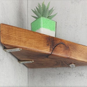 May include: A triangular wooden shelf with a natural wood finish and brass brackets. A small green succulent plant is sitting on the shelf.