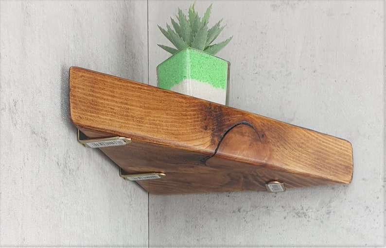 May include: A triangular wooden shelf with a natural wood finish and brass brackets. A small green succulent plant is sitting on the shelf.