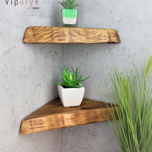May include: Two wooden corner shelves with a rustic finish. The shelves are triangular and have a natural wood grain. The top shelf has a small green plant in a clear glass container. The bottom shelf has a small green plant in a white ceramic pot. The shelves are mounted on a gray concrete wall.