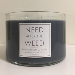 May include: A black glass candle jar with a white label that reads "NEED AFTER THE WEED FIREWOOD SCENTED CANDLE HANDMADE IN MILWAUKEE WI CRUDE CANDLES".