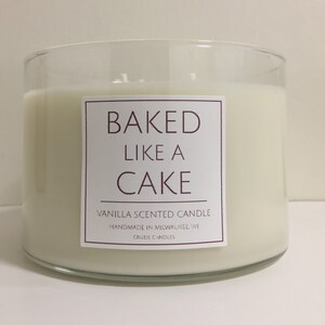 May include: A clear glass candle jar with a white label that reads "BAKED LIKE A CAKE" and "VANILLA SCENTED CANDLE" with the text "HANDMADE IN MILWAUKEE, WI" and "CRUDE CANDLES" below.