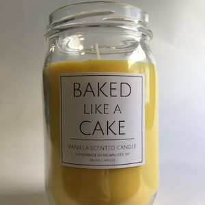 Puede incluir: Una vela perfumada de vainilla amarilla en un frasco de vidrio transparente con una etiqueta blanca que dice "BAKED LIKE A CAKE" y "Vanilla Scented Candle Handmade in Milwaukee, WI Crude Candles".