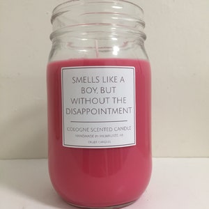 Puede incluir: Una vela rosa en un tarro de vidrio con una etiqueta blanca que dice "Huele como un chico, pero sin la decepci&oacute;n." La etiqueta tambi&eacute;n dice "Cologne Scented Candle, Handmade in Milwaukee, WI, Crude Candles."