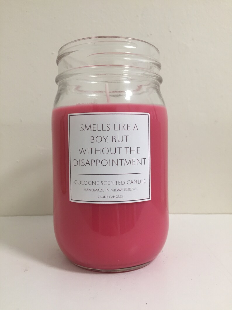 Puede incluir: Una vela rosa en un tarro de vidrio con una etiqueta blanca que dice "Huele como un chico, pero sin la decepci&oacute;n." La etiqueta tambi&eacute;n dice "Cologne Scented Candle, Handmade in Milwaukee, WI, Crude Candles."