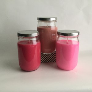 Puede incluir: Tres frascos de vidrio con tapas que contienen velas rosadas, rojas y marr&oacute;n claro. Los frascos est&aacute;n sobre una superficie con un patr&oacute;n blanco y negro.