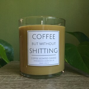 May include: A brown coffee scented candle in a clear glass jar with a white label that reads "Coffee But Without Shitting" and "Coffee Scented Candle Handmade in Milwaukee, WI Crude Candles".