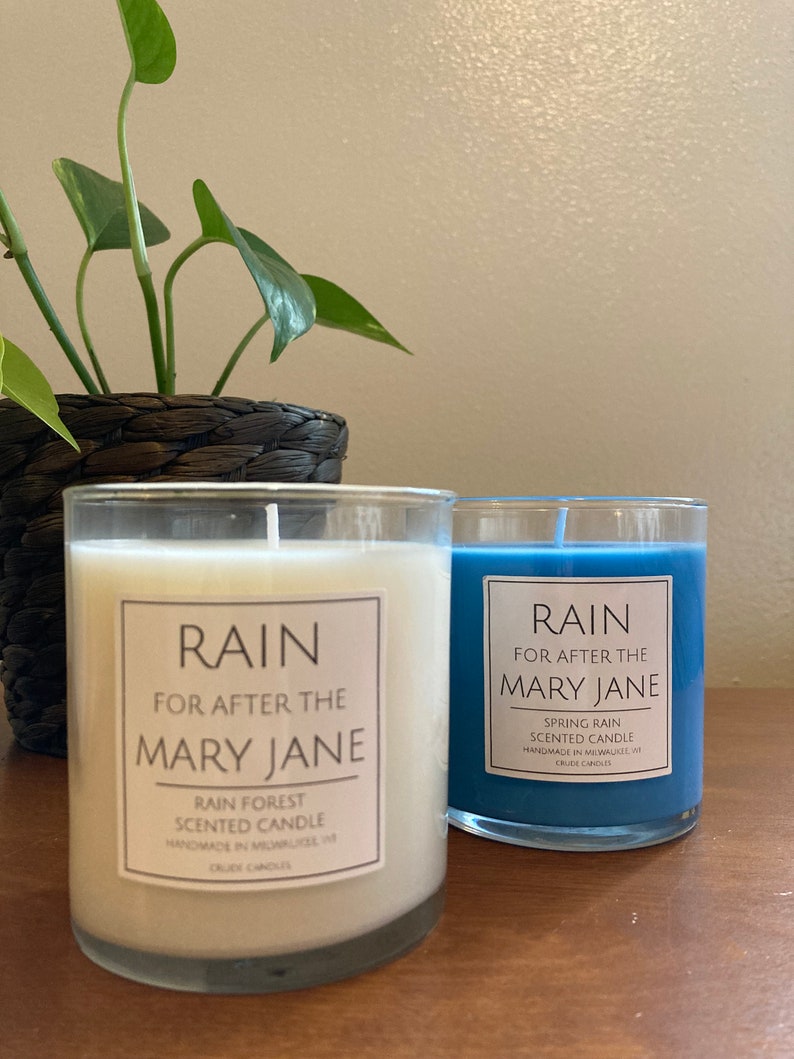K&ouml;nnte beinhalten: Zwei Glaskerzenbeh&auml;lter mit wei&szlig;em und blauem Wachs. Die Beh&auml;lter tragen Etiketten mit der Aufschrift "RAIN FOR AFTER THE MARY JANE" und "SPRING RAIN SCENTED CANDLE HANDMADE IN MILWAUKEE, WI CRUDE CANDLES".