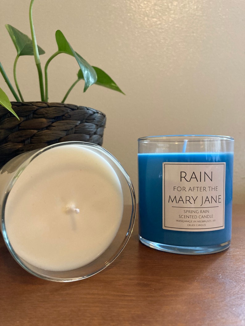 K&ouml;nnte beinhalten: Zwei Kerzen, eine mit blauem Wachs und die andere mit wei&szlig;em Wachs. Die blaue Kerze hat ein Etikett mit der Aufschrift "RAIN FOR AFTER THE MARY JANE SPRING RAIN SCENTED CANDLE HANDMADE IN MILWAUKEE, WI CRUDE CANDLES".