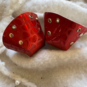 Puede incluir: Dos tazas de metal rojo con un patrón de corazón y detalles dorados. Las tazas tienen un fondo redondeado y una parte superior acampanada.