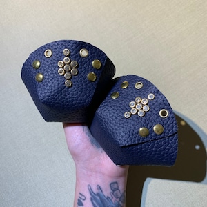 May include: Two dark blue leather pouches with gold studs and rhinestones. The pouches are shaped like a half-circle and have a decorative design of rhinestones in the centre.