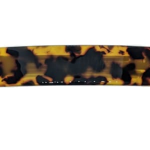 May include: Rectangular hair barrette with a tortoiseshell pattern. The barrette features a mix of dark brown and amber tones, creating a marbled effect. The accessory is designed to hold hair in place and adds a decorative element.