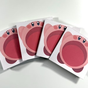 May include: Four square stickers featuring a pink cartoon character with a large open mouth, small blue eyes, and small arms. The character is set against a white background. The stickers are slightly angled, creating a sense of depth.