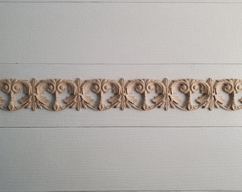 May include: A decorative wooden trim with a repeating pattern of ornate scrolls and leaves. The trim is a light brown color and has a smooth finish.