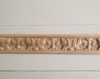 May include: A close-up of a wooden trim molding with a decorative, carved design. The molding features a repeating pattern of stylized leaves and swirls.