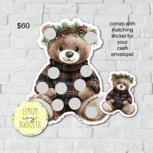 May include: A large and small bear-shaped sticker set. The bears wear plaid sweaters and pinecone wreaths. The large bear has several scratch-off circles. The set includes a matching sticker for cash envelopes. The Lemon Ivy Budgets logo is also visible.