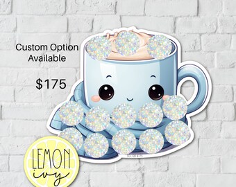 May include: A blue cartoon mug with a smiling face, wearing a blue scarf and topped with white whipped cream. The mug is surrounded by white glitter circles. The text "Custom Option Available $175" is visible in the top left corner. The text "LEMON ivy" is visible in the bottom left corner.