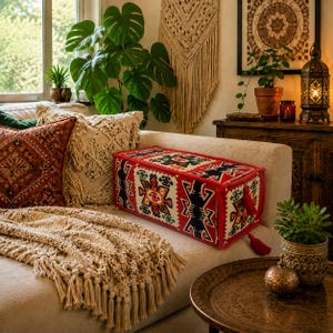 May include: A rectangular bolster pillow featuring a vibrant red base with intricate geometric patterns in black, white, orange, and green. The pillow is finished with red piping along the edges and includes decorative red tassels on the side.