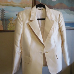 Op de afbeelding: Een cr&egrave;mekleurige blazer met een enkele knoopsluiting. De blazer hangt aan een zwarte hanger.