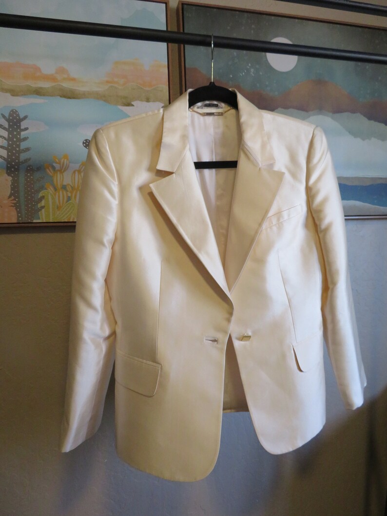 Op de afbeelding: Een cr&egrave;mekleurige blazer met een enkele knoopsluiting. De blazer hangt aan een zwarte hanger.