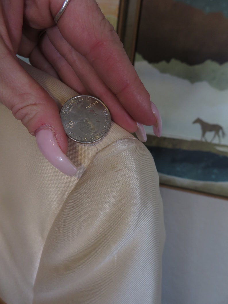Op de afbeelding: Close-up van een witte stof met een Amerikaanse kwart dollar erop. De stof heeft een subtiele textuur en een lichte glans.