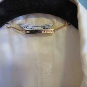 Op de afbeelding: Een wit overhemd met een gouden ketting en een label met de tekst "Made in Italy" en "VERSACE".