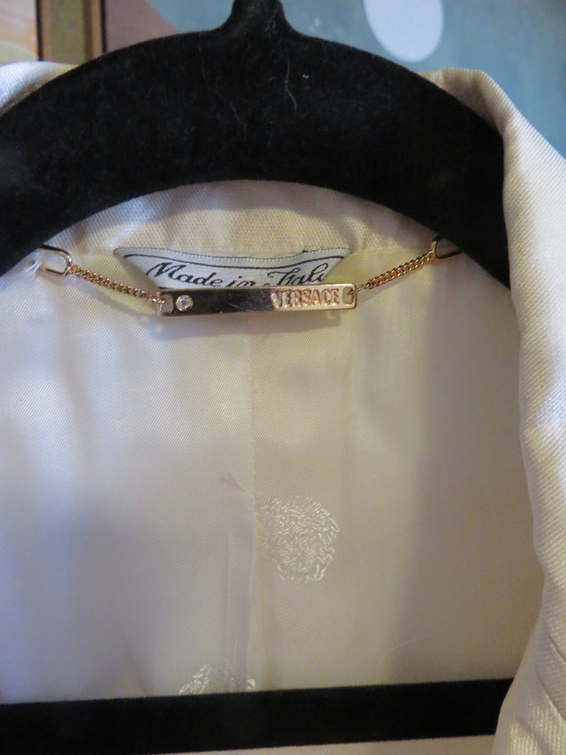 Op de afbeelding: Een wit overhemd met een gouden ketting en een label met de tekst "Made in Italy" en "VERSACE".