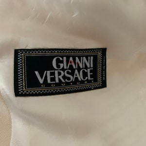 Op de afbeelding: Een wit label met zwarte tekst die "Gianni Versace Couture" en "Made in Italy" zegt.