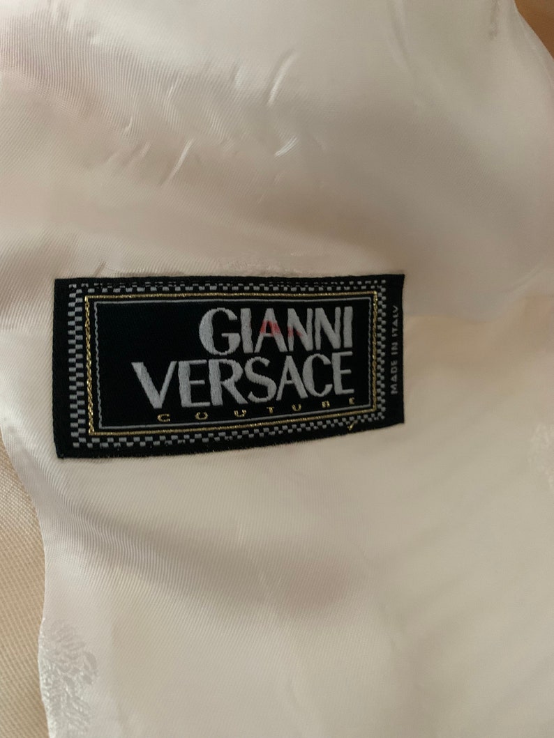 Op de afbeelding: Een wit label met zwarte tekst die "Gianni Versace Couture" en "Made in Italy" zegt.