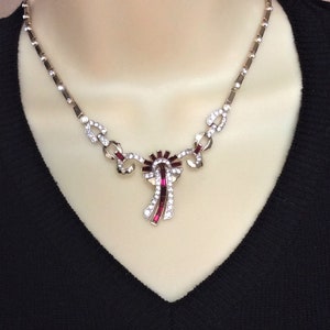 May include: A gold necklace with a pendant featuring a geometric design with red and clear rhinestones.