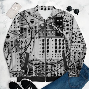May include: A black and white bomber jacket featuring a detailed pattern of electronic components, wires, and knobs. The jacket has a zipper closure, black pockets, and a ribbed hem. The design is a grayscale image of a modular synthesizer.